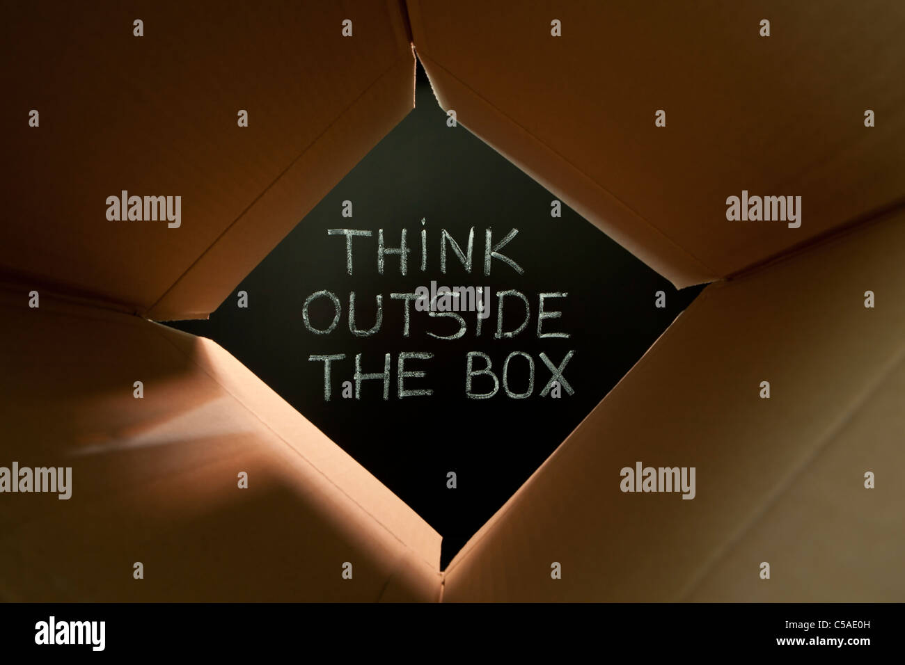 Concept image about unconventional or different thinking. 'Think outside the box' handwritten with white chalk on a blackboard. Stock Photo
