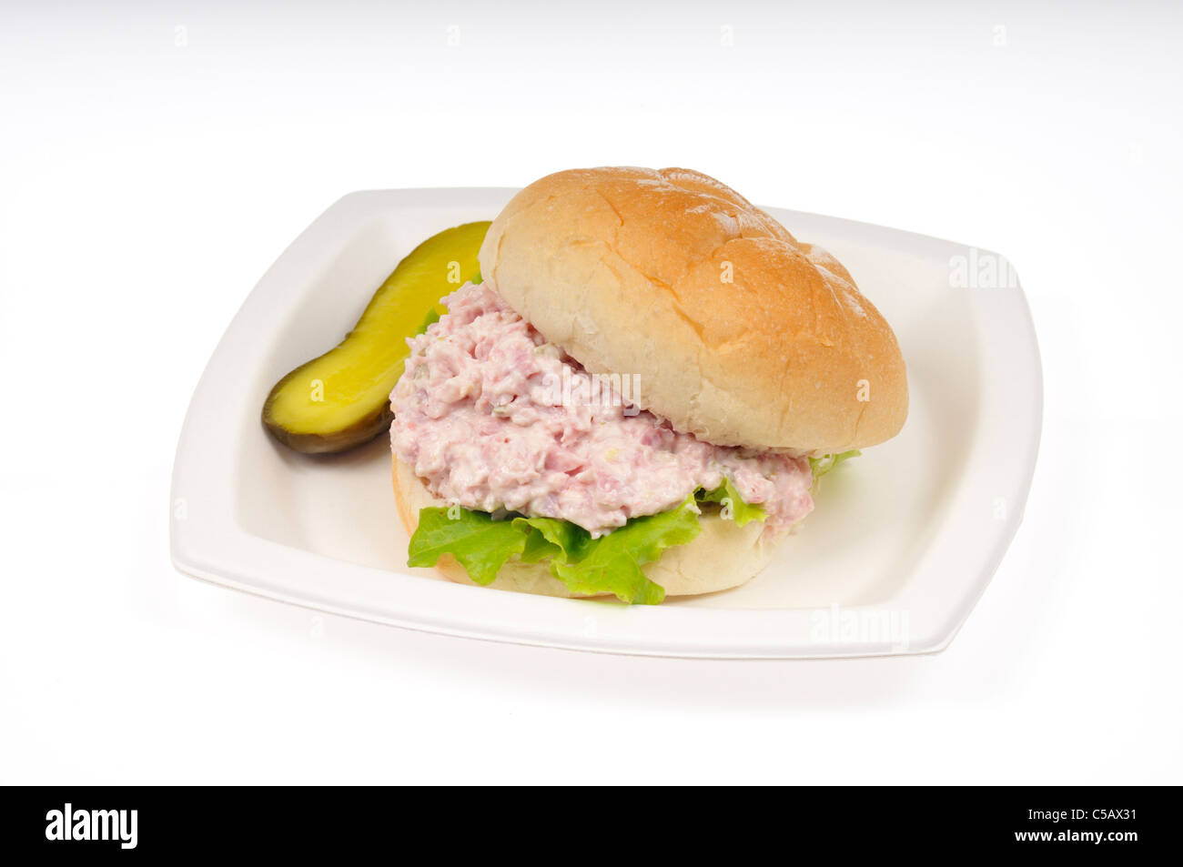 Ham salad sandwich in a roll with lettuce and a pickle on white plate on white background, cut out. Stock Photo