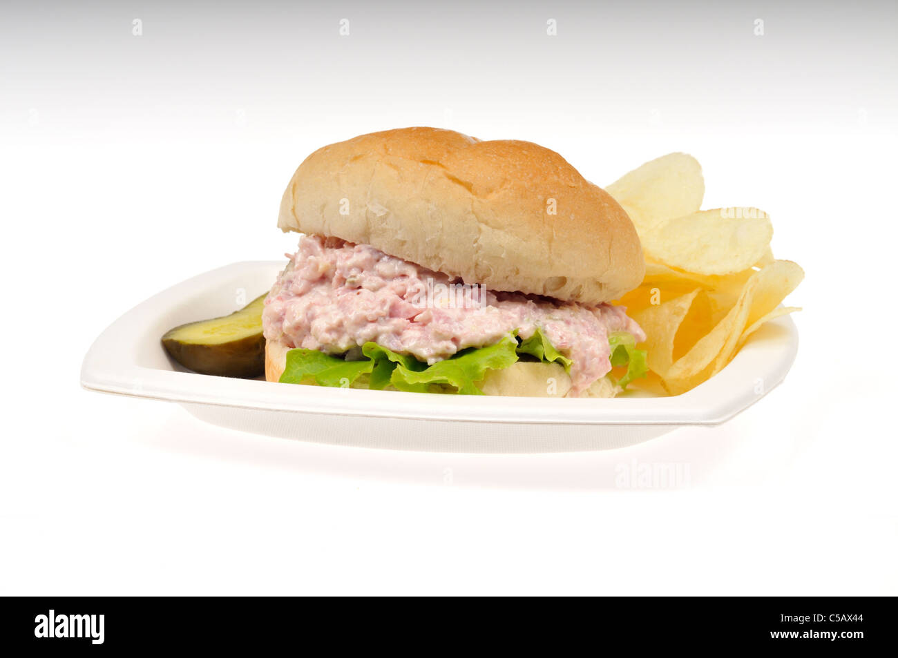 Ham salad with lettuce sandwich in a roll with potato chips and  a pickle on white plate on a white background, cut out. Stock Photo