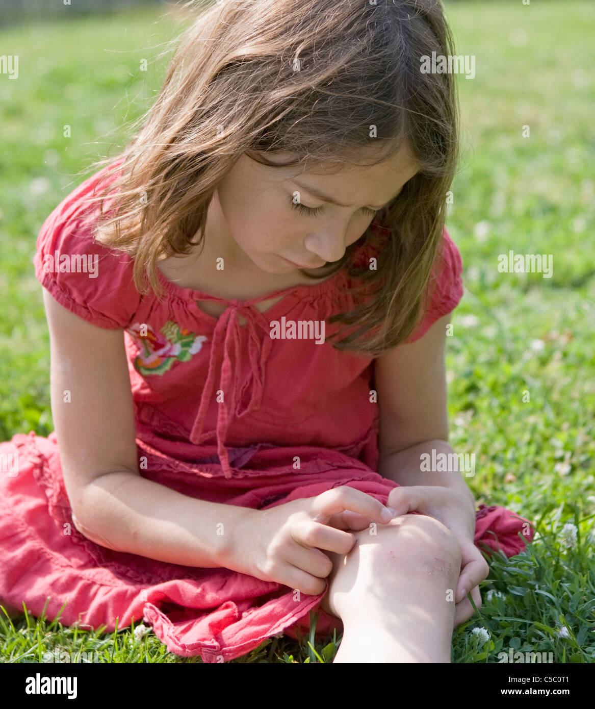A young girl examines her scraped knee from a bicycle accident the day