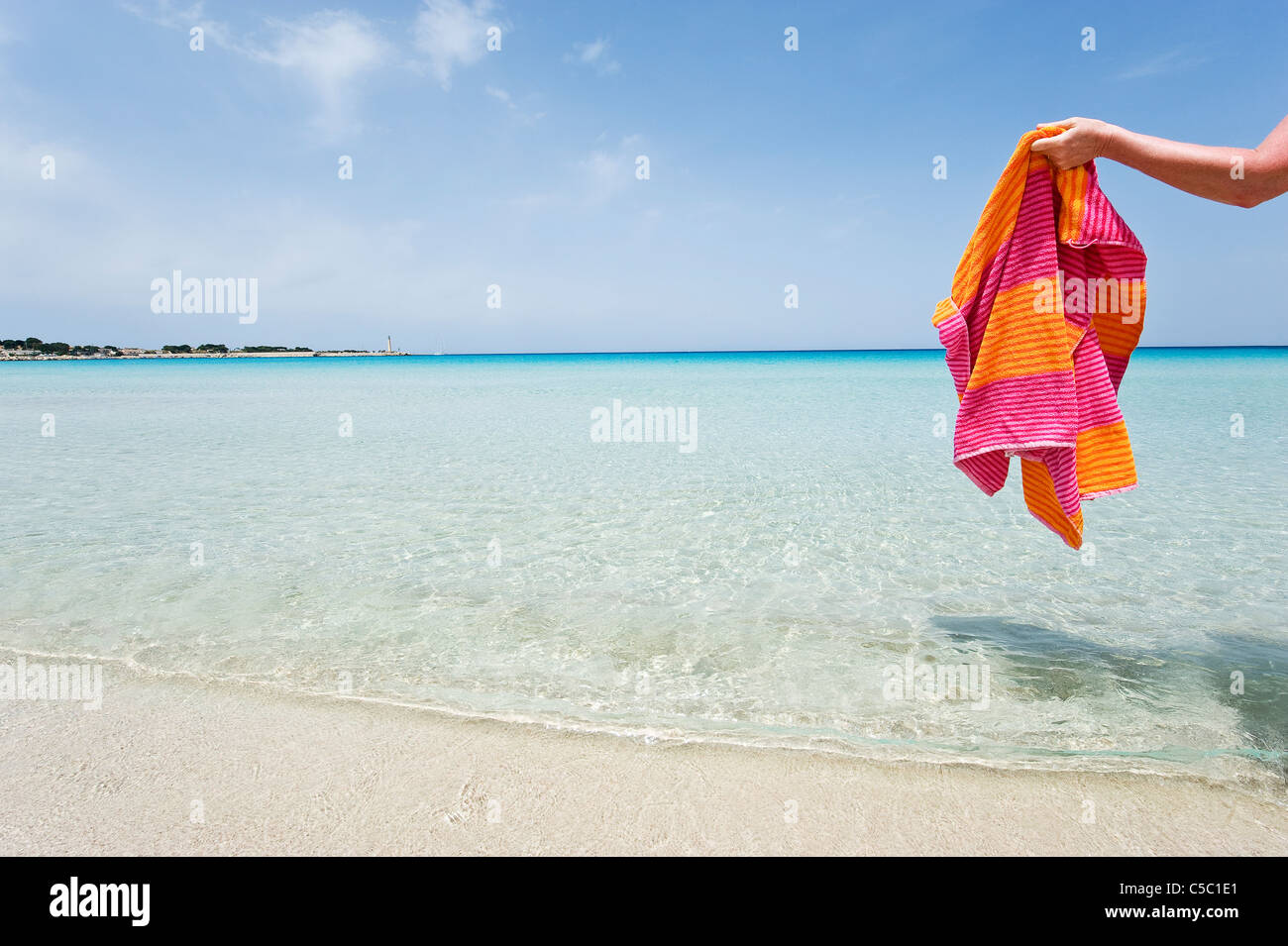 Hand holding towel at water's edge on a peaceful beach Stock Photo