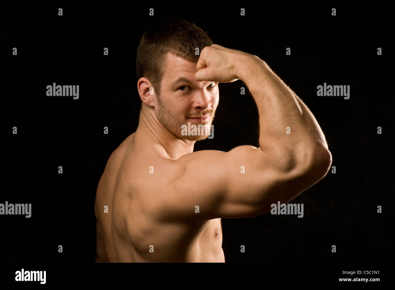 Close-up portrait of smiling macho man flexing muscles over black background Stock Photo