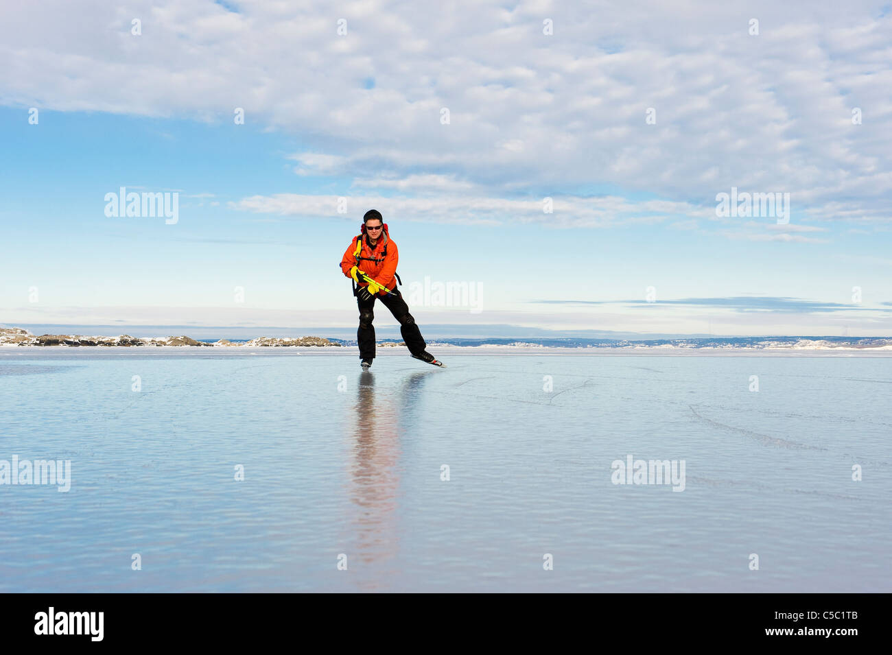Skater on peaceful frozen lake below cloudy sky Stock Photo