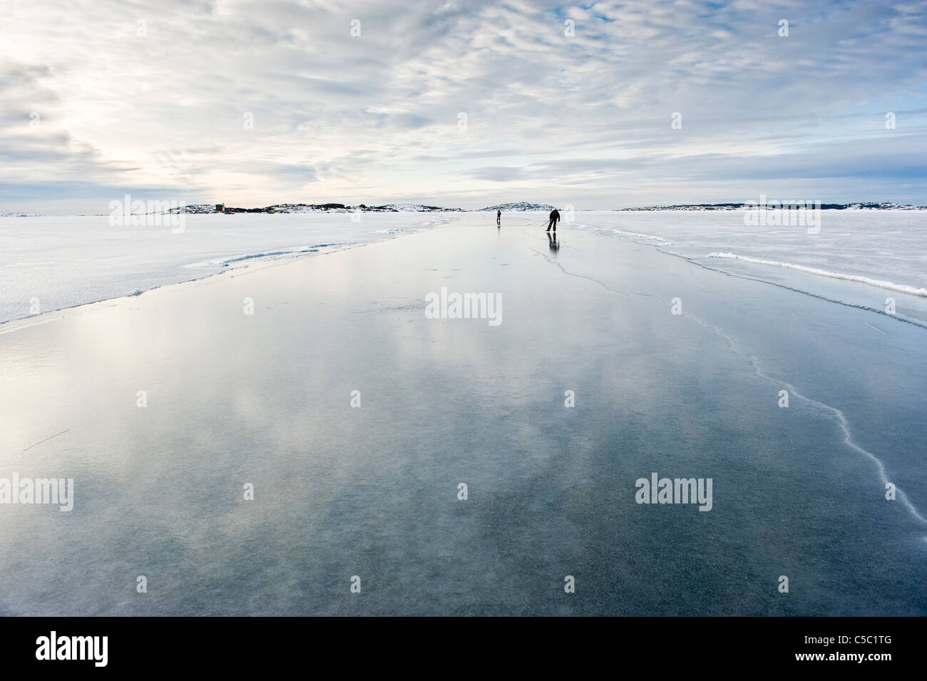 Distance shot of two skaters on peaceful frozen lake below cloudy sky Stock Photo