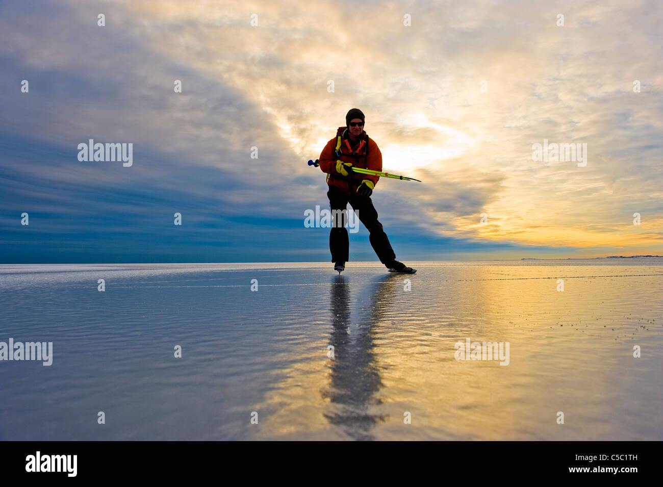 Skater on peaceful frozen lake against scenic shot of sunset Stock Photo
