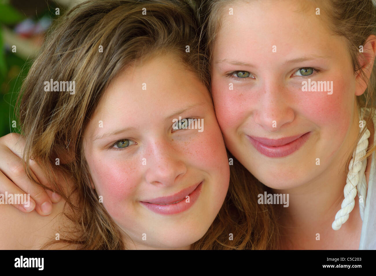 Close-up portrait of two twin sisters with arm around shoulder smiling Stock Photo