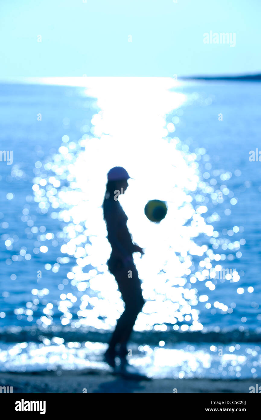 Side view of a silhouette teenage girl with football against the glittering sea Stock Photo