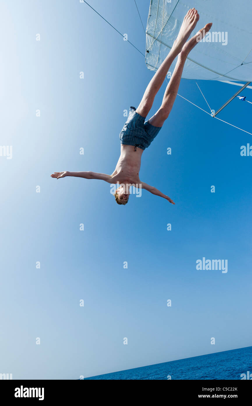 Low angle view of a shirtless boy diving from sailboat against clear blue sky Stock Photo