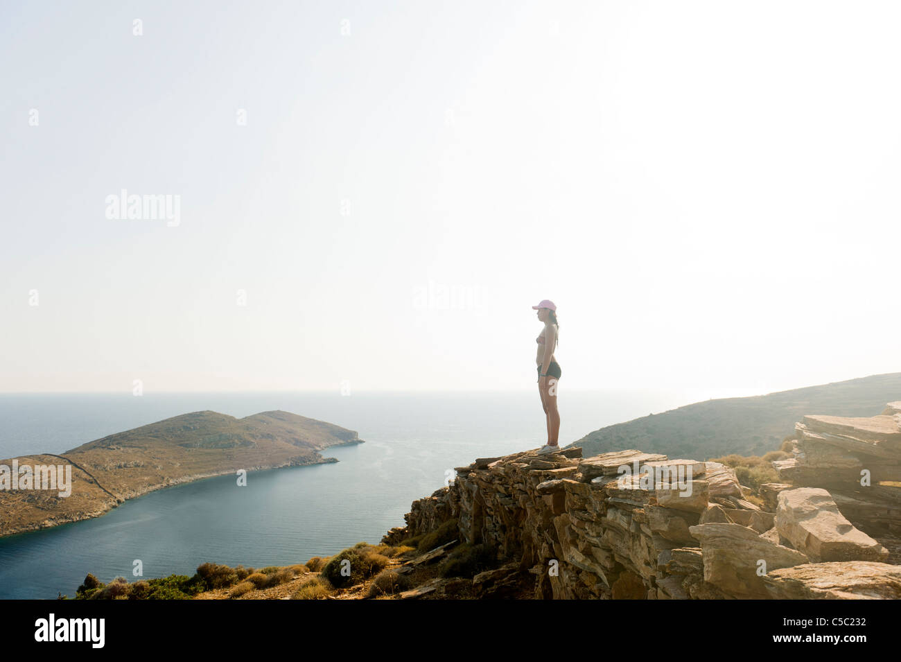 Side view of a teenage girl standing on cliff by the peaceful sea against clear sky Stock Photo