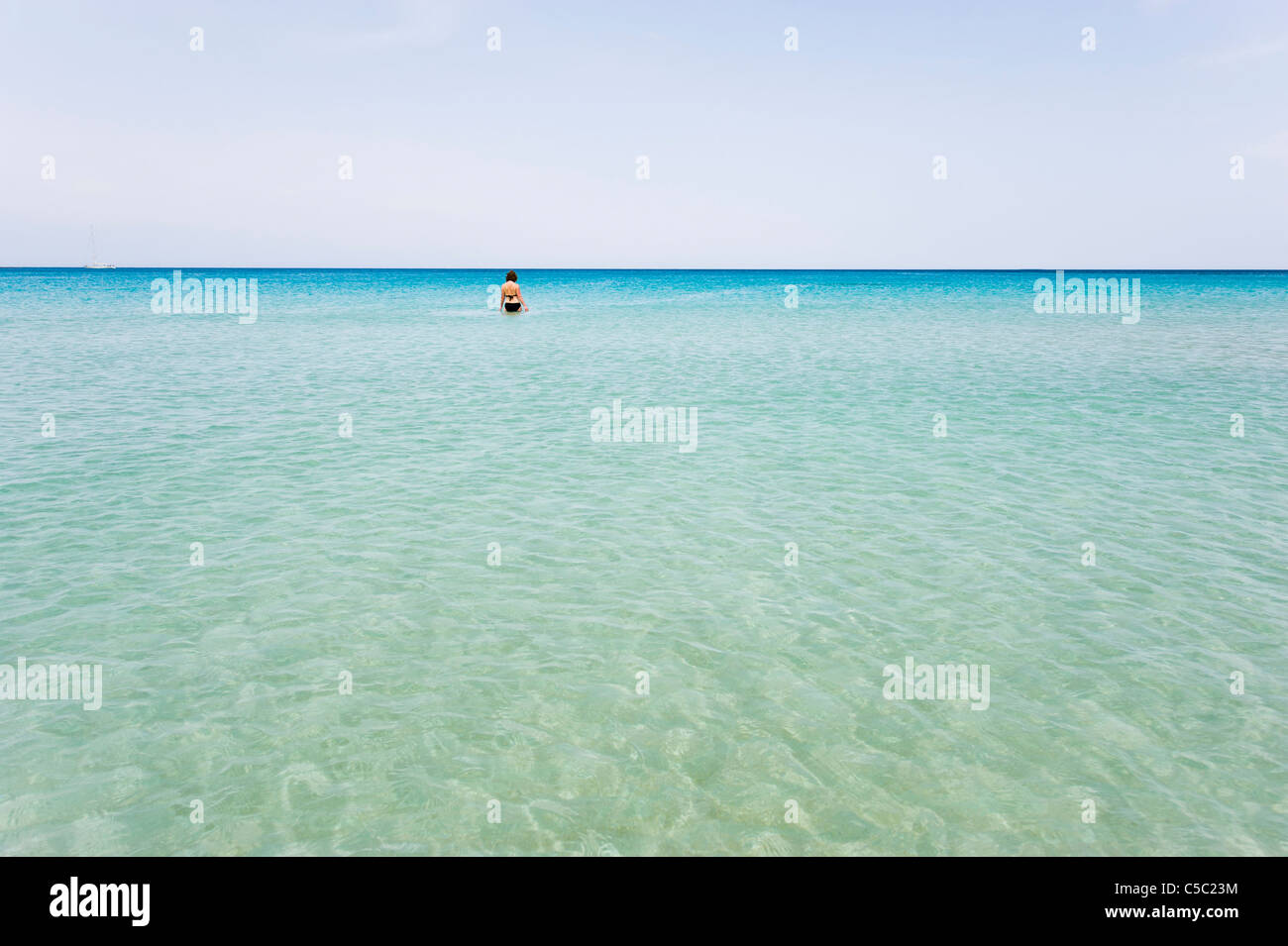 Beach with clear and peaceful water with woman at a distance against clear sky Stock Photo