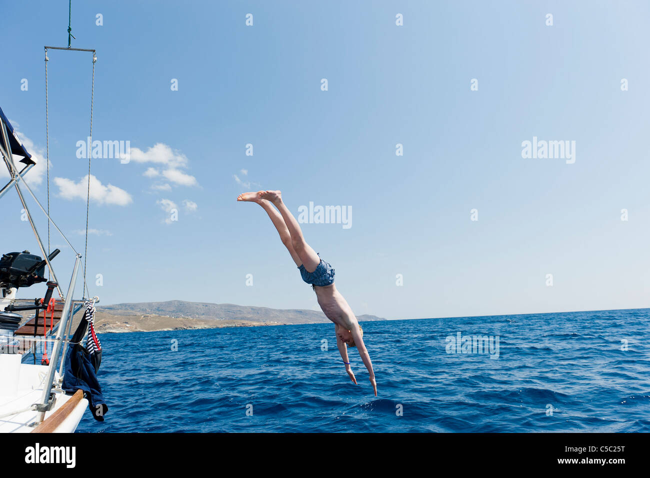 Shirtless teenage boy dives from a sailboat into the water against clear sky Stock Photo