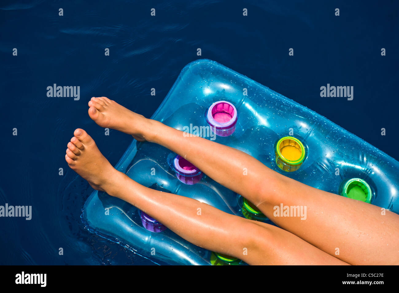 Beautiful woman's legs with bare feet on air mattress in the water Stock Photo