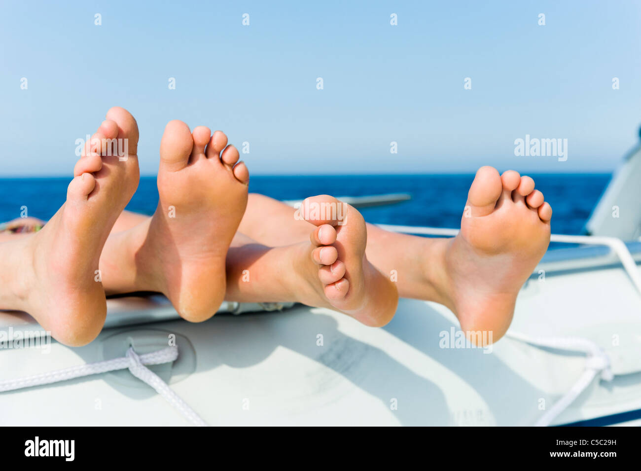 Close-up of bare feet on the sailboat with sea against clear sky Stock Photo