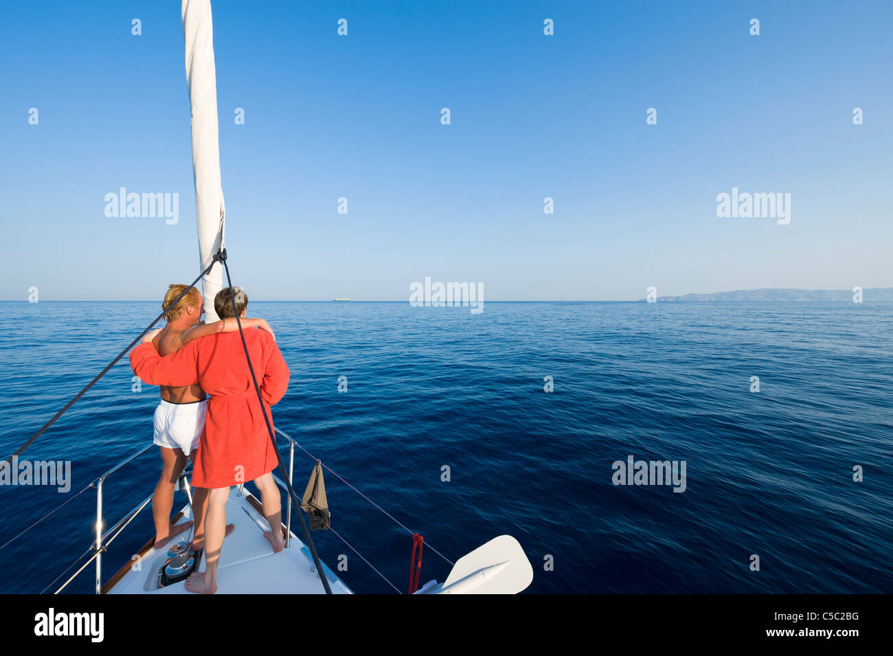 Rear view of teenage couple on the boat overlooking the blue sea against clear sky Stock Photo