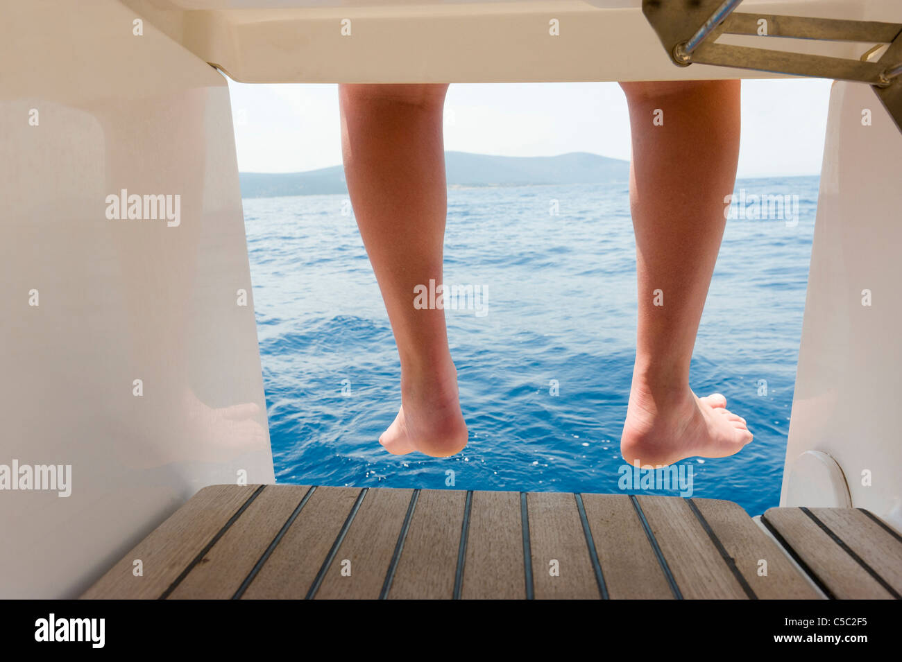 Close-up of bare feet on the sailboat against blue water Stock Photo