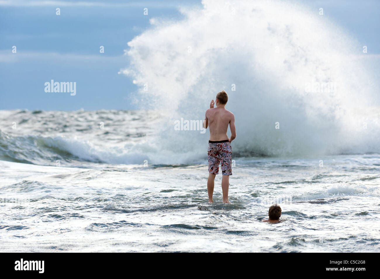 Rear view of young man in front of a big wave in the sea Stock Photo