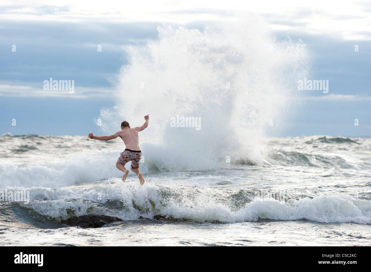 Rear view of a shirtless teenage boy jumping in big waves at sea Stock Photo