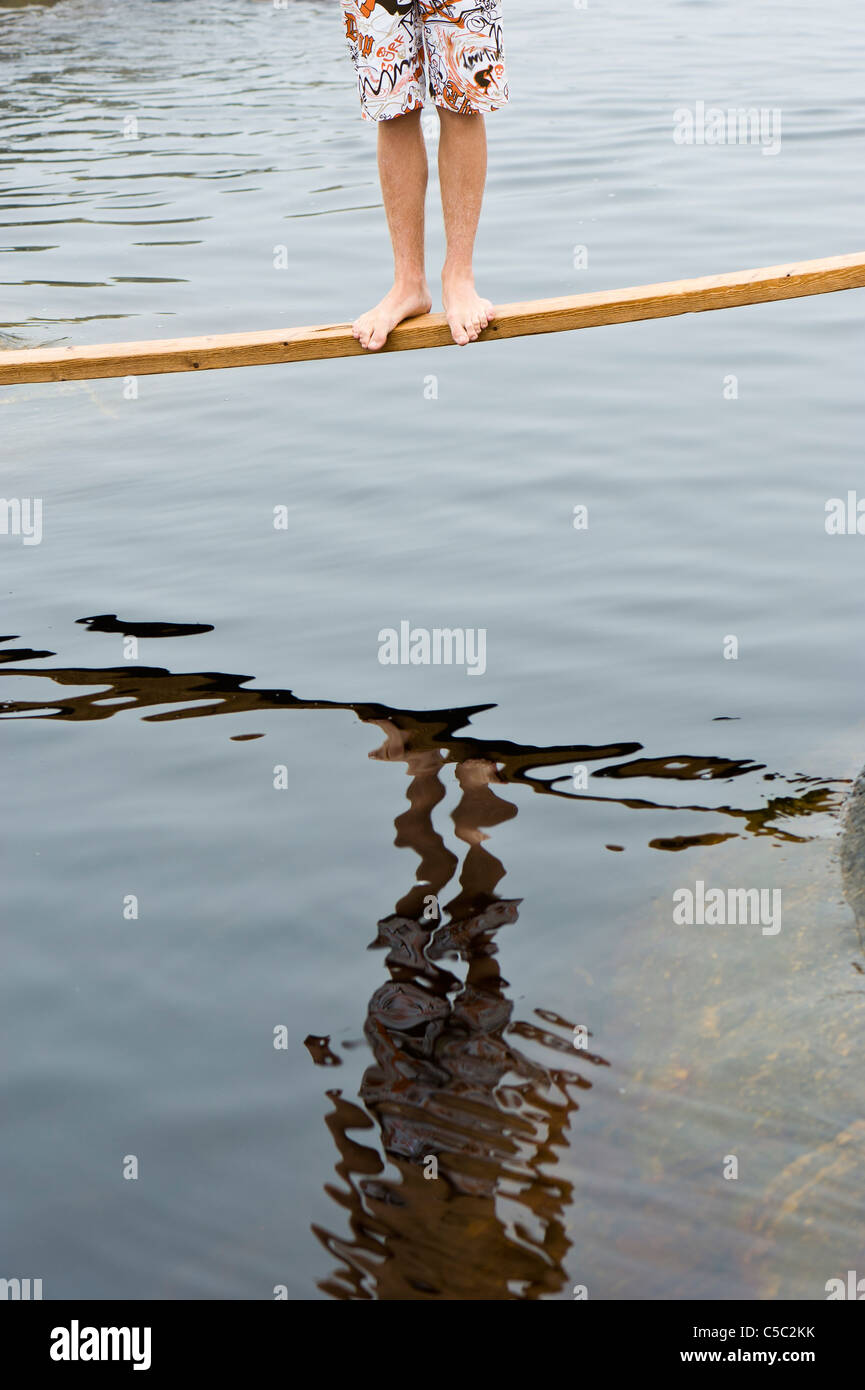 Low section of bare feet standing on a plank over the water Stock Photo
