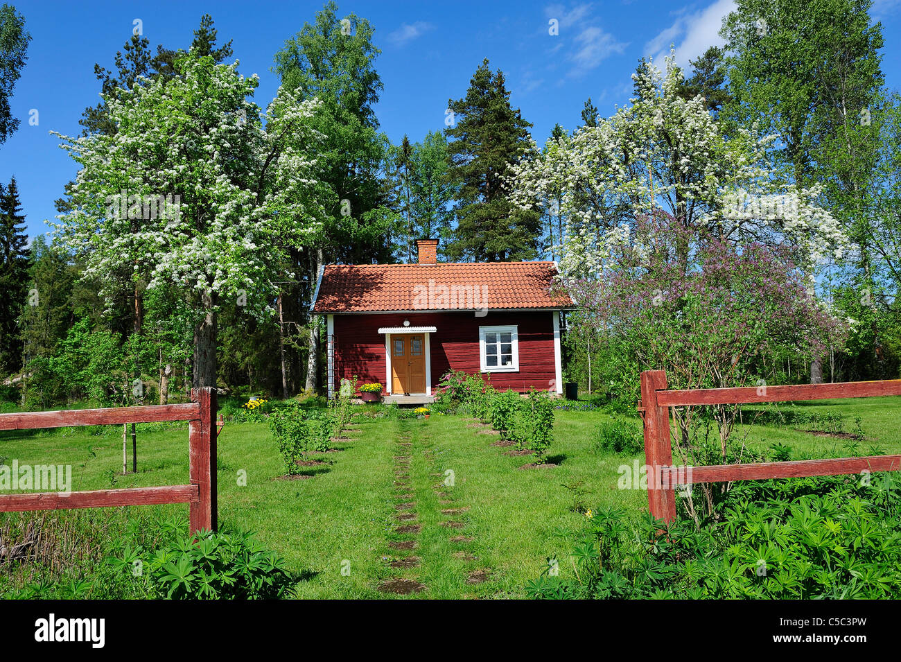 Entrance of a fenced small red cottage against trees Stock Photo
