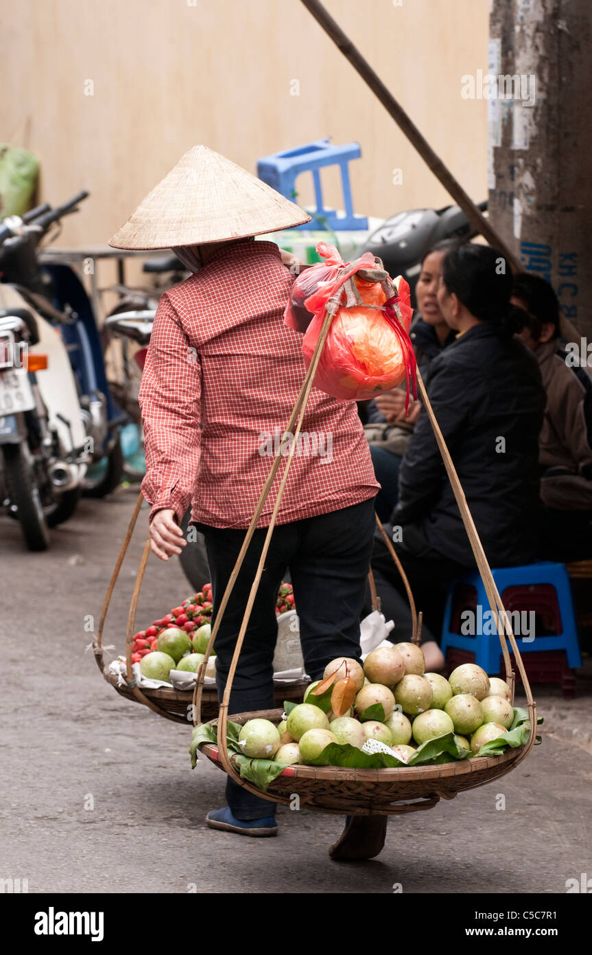 Street hawker carrying baskets of fruit, Hang Buom St, Hanoi Old Quarter, Vietnam Stock Photo