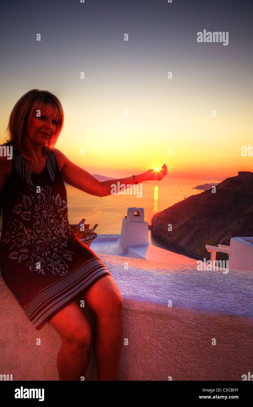 Warning - noisy image due to HDR - Lady holds the sun in her hand as it sets, sunset Thira Santorini Stock Photo