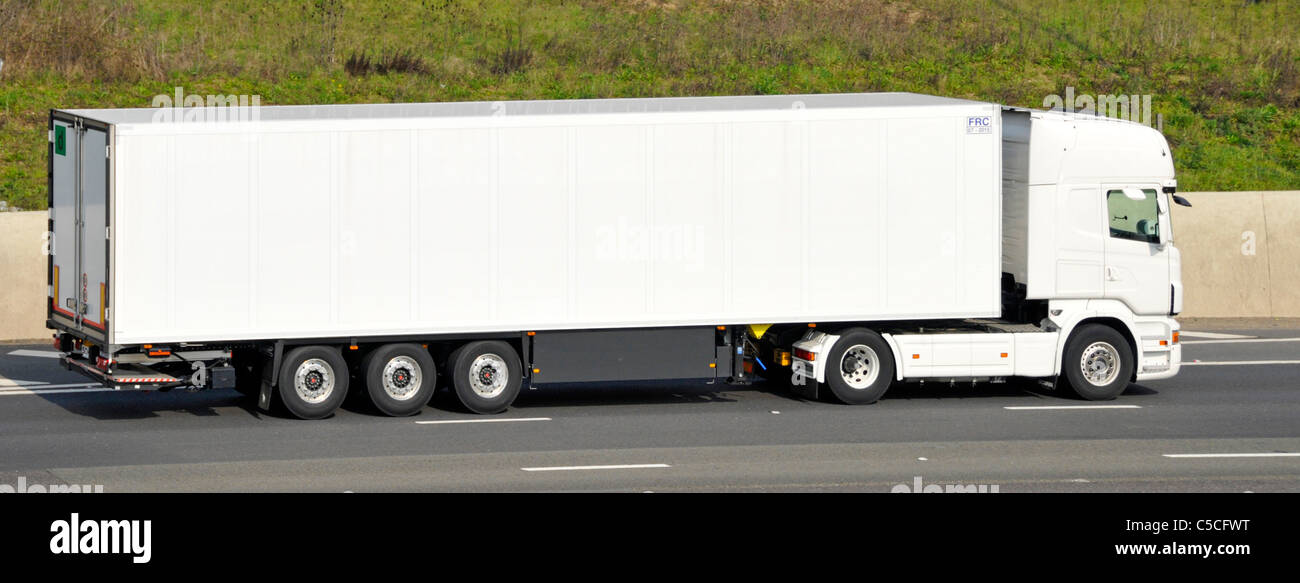Transport business side view of all white long clean unmarked big hgv lorry truck and articulated trailer driving along M25 motorway England UK Stock Photo