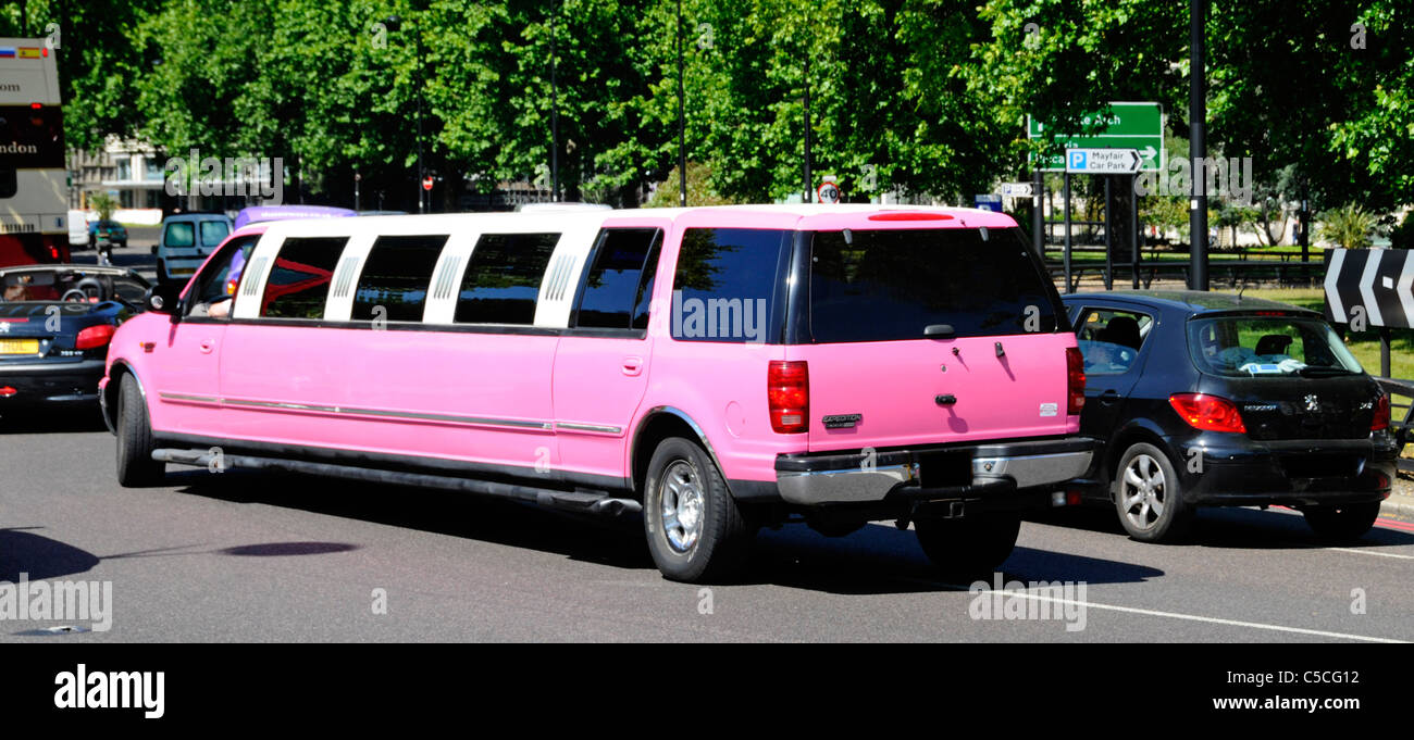 London street scene side and rear back view of pink stretch Limo luxury car transport limousine dark windows driving on Park Lane Mayfair England UK Stock Photo