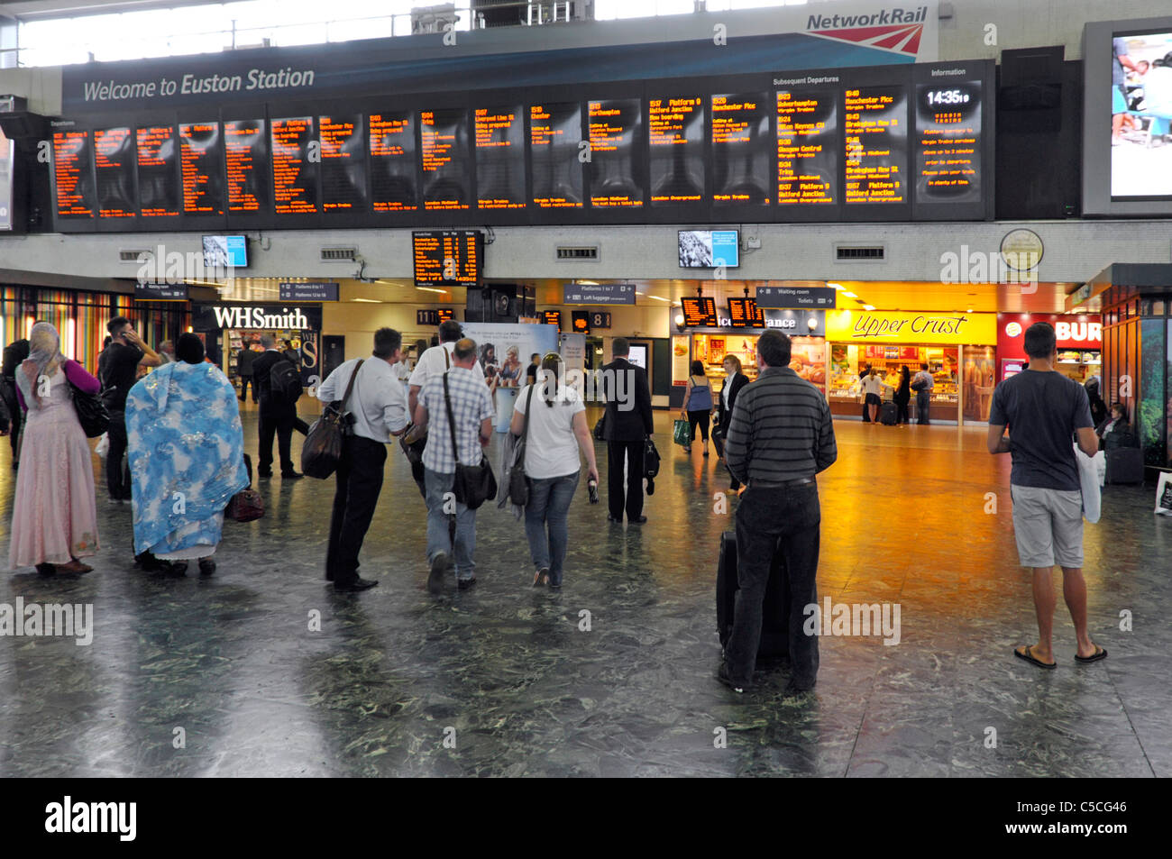 Euston railway train station concourse back view travellers viewing train departure information board shops beyond London England UK Stock Photo