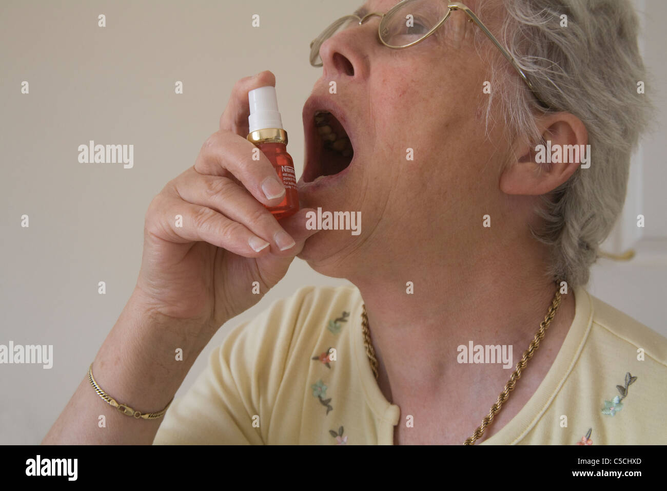 Elderly woman using a Nitrolingual pump spray to ease pain after heart attack Stock Photo