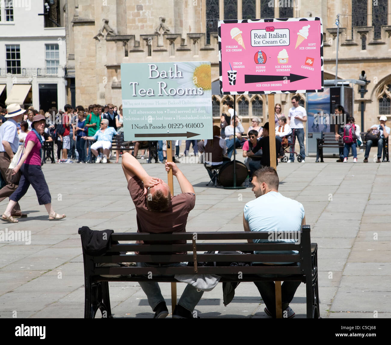 Men holding advertising boards sit on bench in the Abbey churchyard, Bath, England Stock Photo