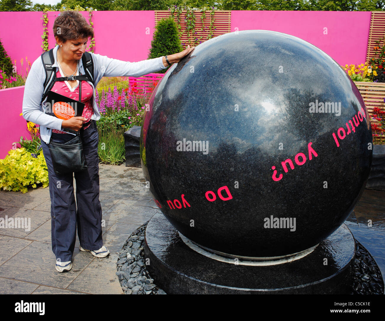 Woman playing with a giant five ton granite sphere, floating on a water-cushioned base, in a conceptual garden. Stock Photo