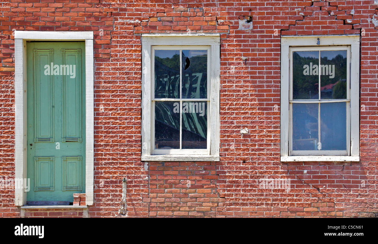 Green Wood Door against a Red Brick Wall with Two White Wood Windows Stock Photo