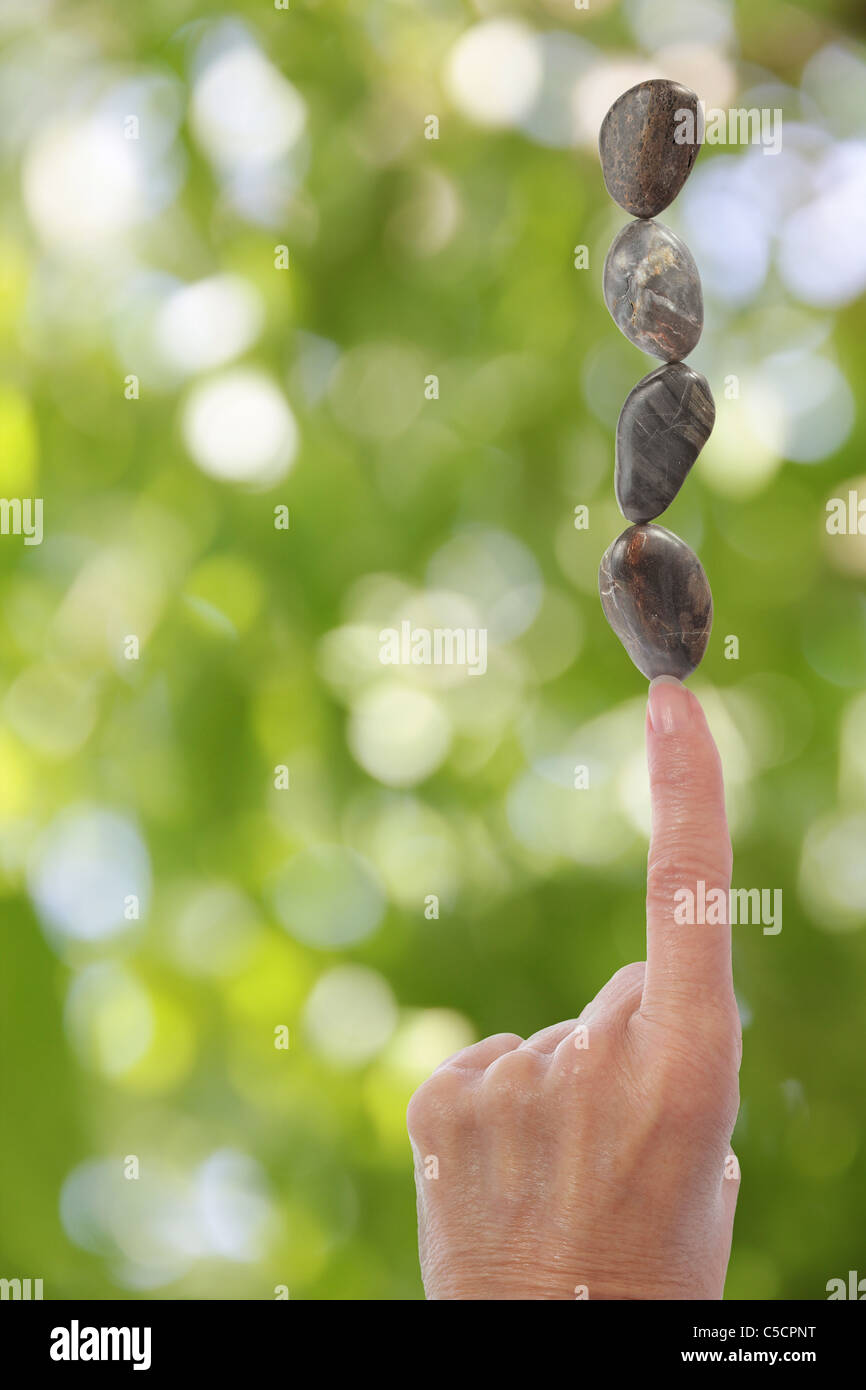 Hand Balance Stones on Finger with Blurred Green Background Stock Photo