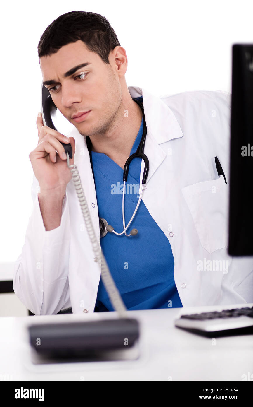 Caucasian male doctor sitting at the desk with computer talking over phone in white background Stock Photo