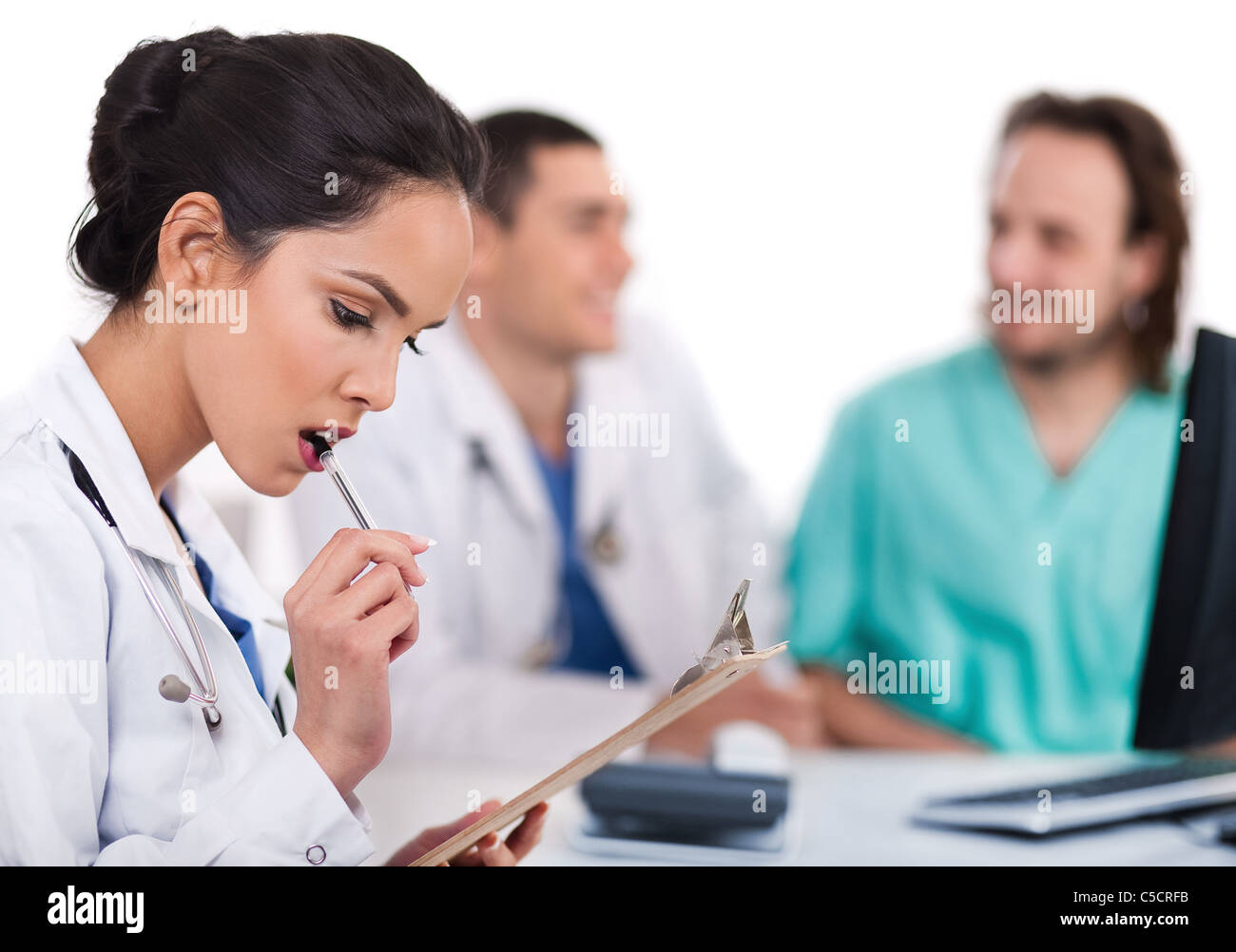 Young asian doctor thinking with the pen, others blurred behind over white background Stock Photo