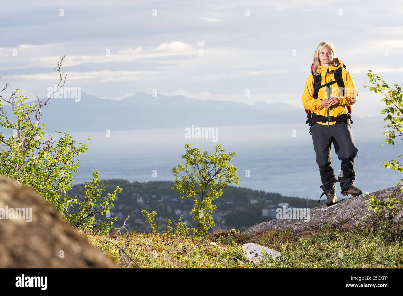Full length portrait of a woman in yellow shell on mountain against clouds Stock Photo