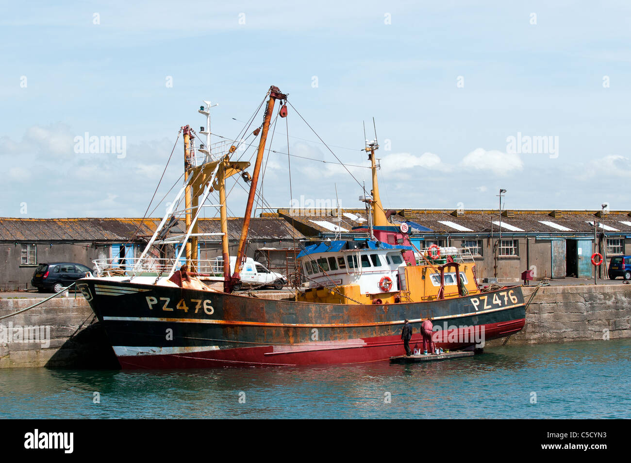 Two workers painting the hull of a fishing trawler tied up in Newlyn Harbour in Cornwall. Stock Photo