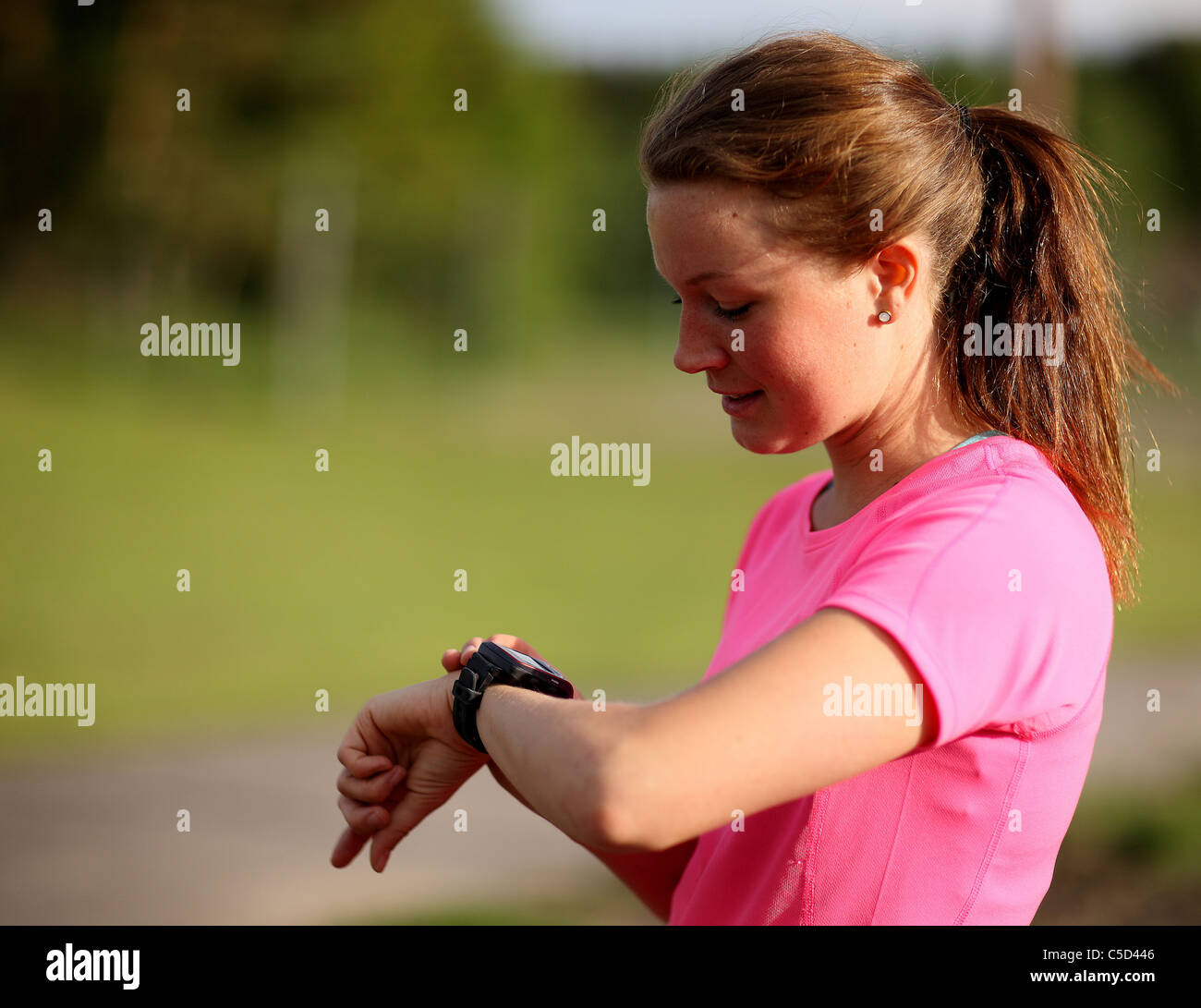 Side view of a brown-haired female runner adjusting heart rate monitor against blurred background Stock Photo