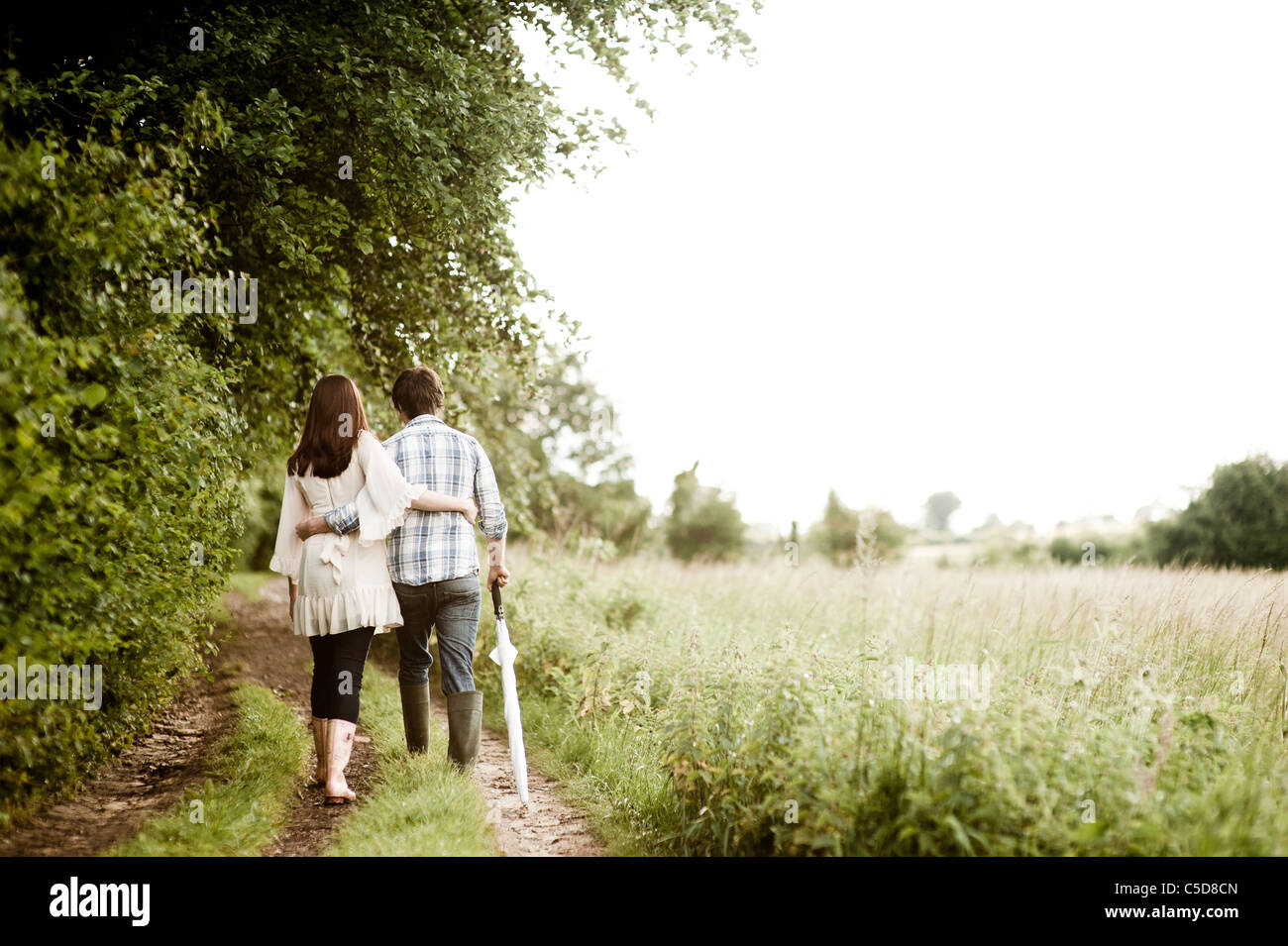 Young couple walking away in a field of grass and trees Stock Photo - Alamy