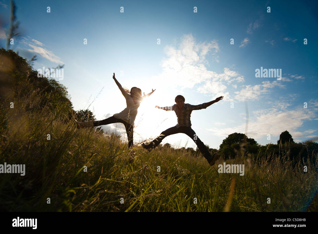 Man and woman star jump in a field silhouetted Stock Photo