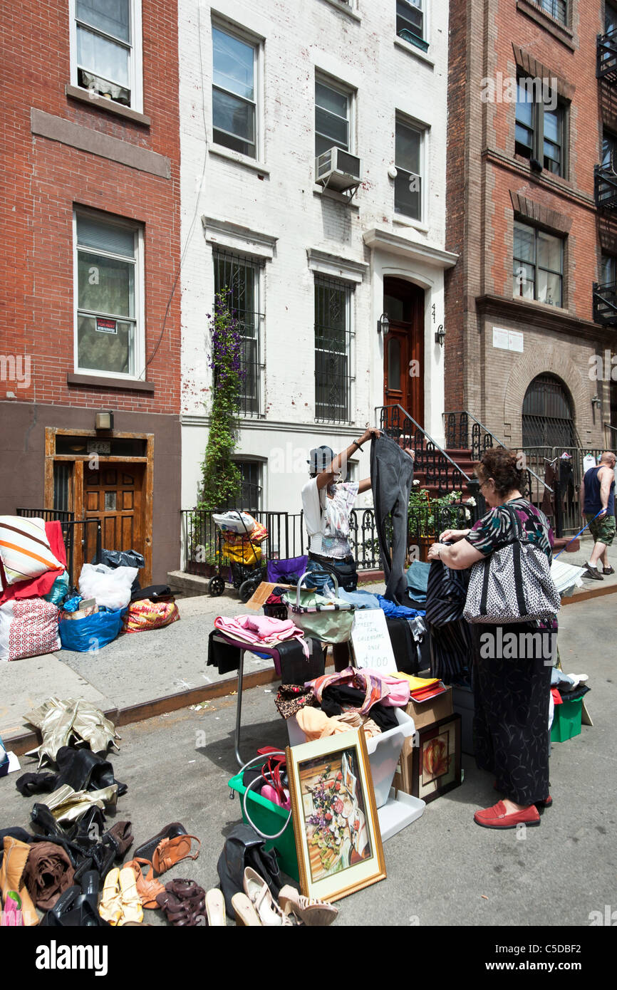 vendor shows off pair of pants for customer amid colorful array of treasures spread along 44th Street in front of old tenements Stock Photo