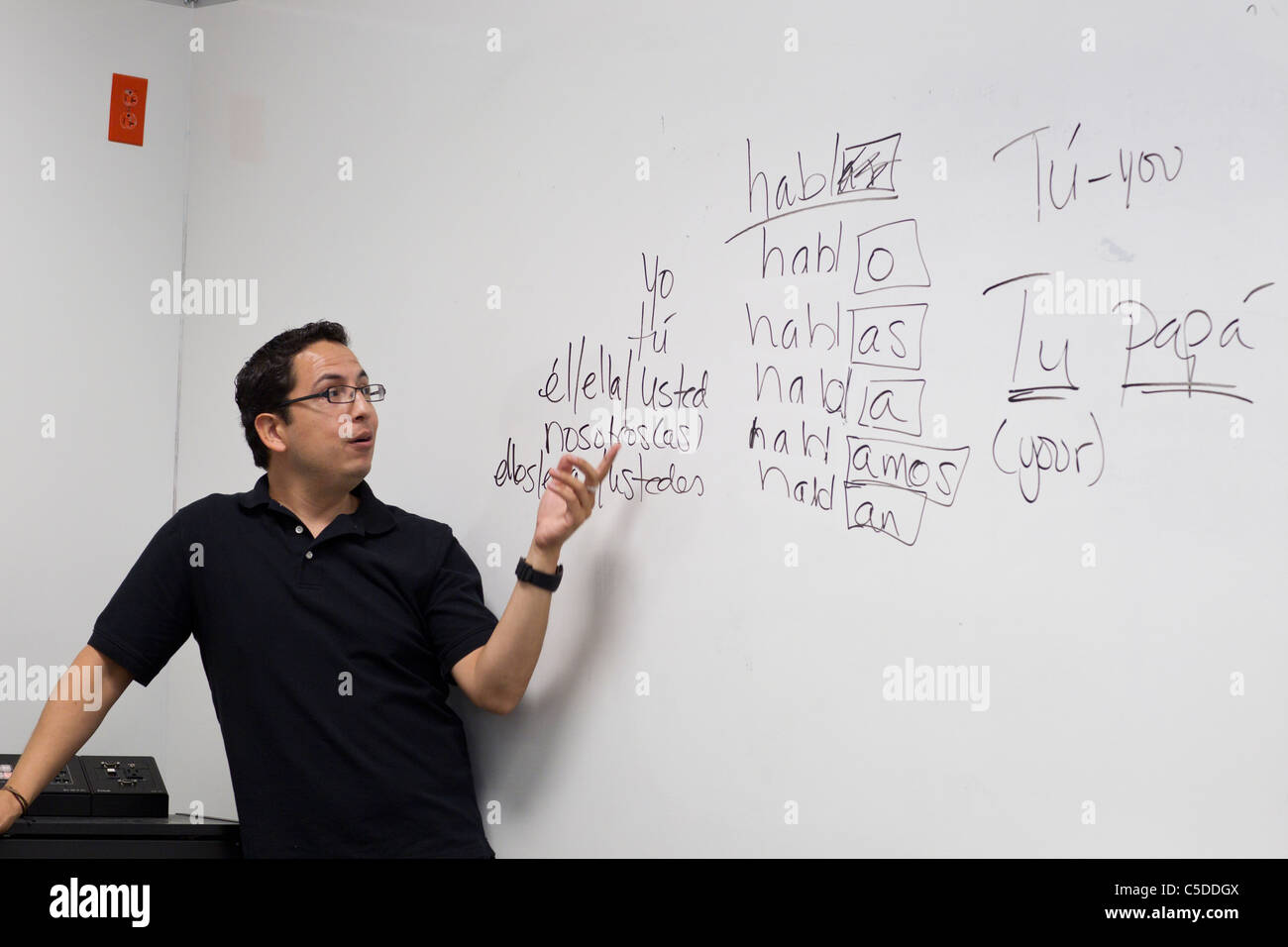 Hispanic male Spanish language teacher points to board with verb conjugations during class in South Texas high school Stock Photo