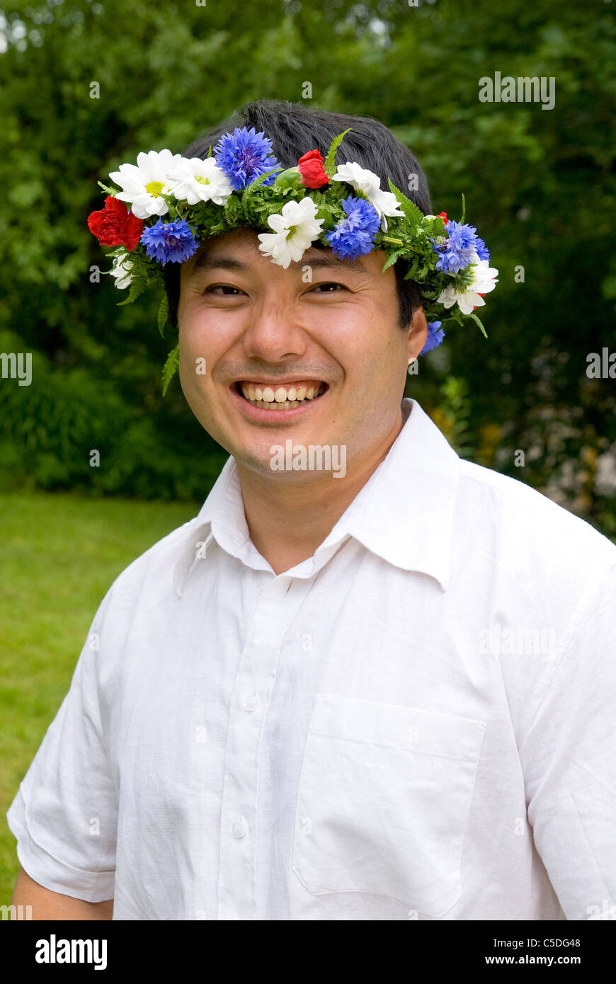 Portrait of an Asian man in floral wreath smiling outdoors Stock Photo