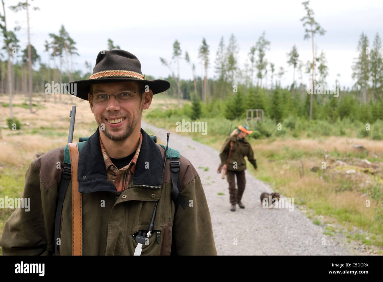 Portrait of a smiling hunter with friend and dog walking on country road in background Stock Photo