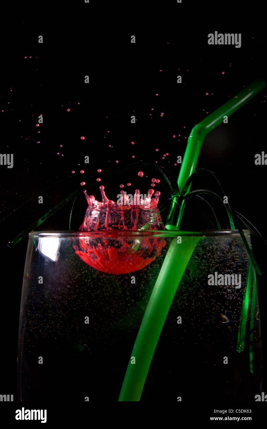 red food coloring being dropped in to a glass of water, with a green drinking straw in the glass. Stock Photo