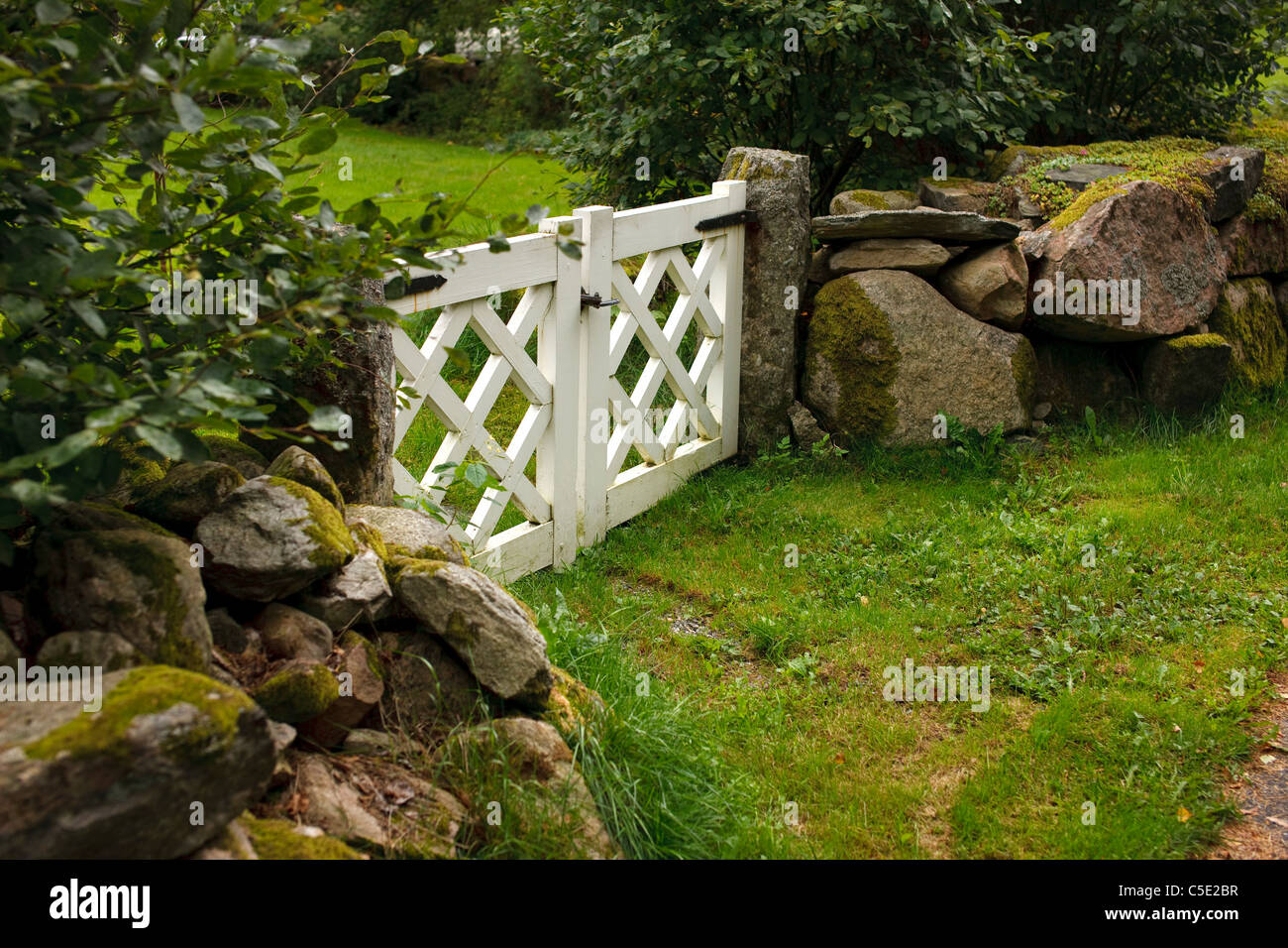 Stone stack wall with white closed gate in the garden Stock Photo