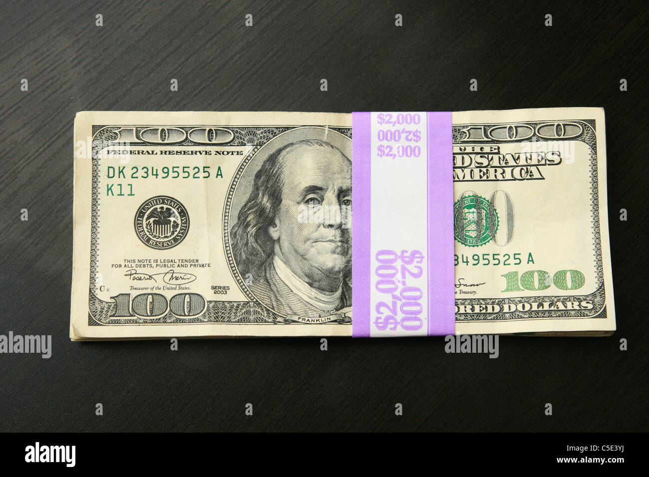 two thousand dollars in 100 bills on a dark wood table top Stock Photo