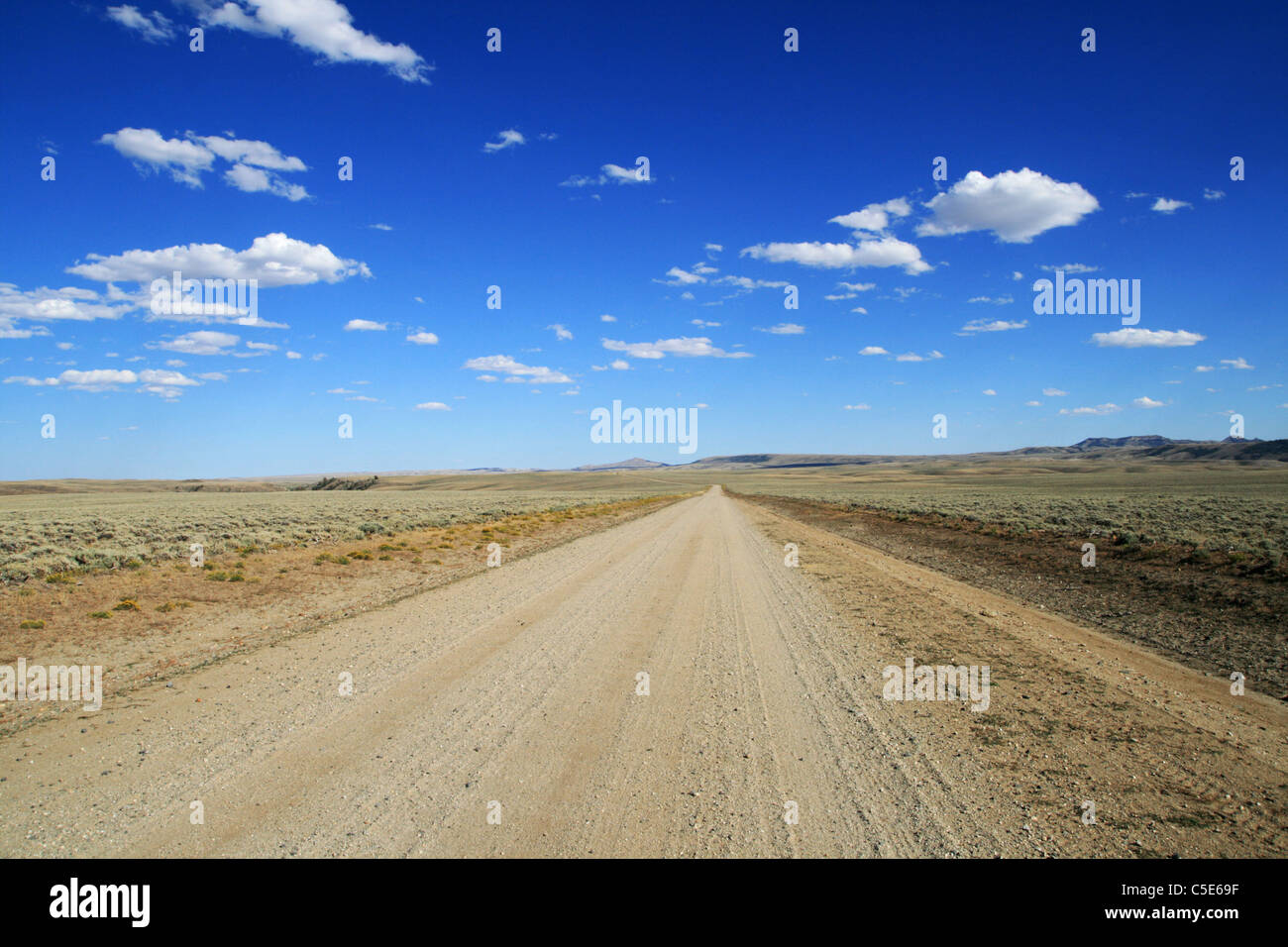 lonely dirt road runs across the Wyoming plains to a distant horizon with blue sky and clouds Stock Photo