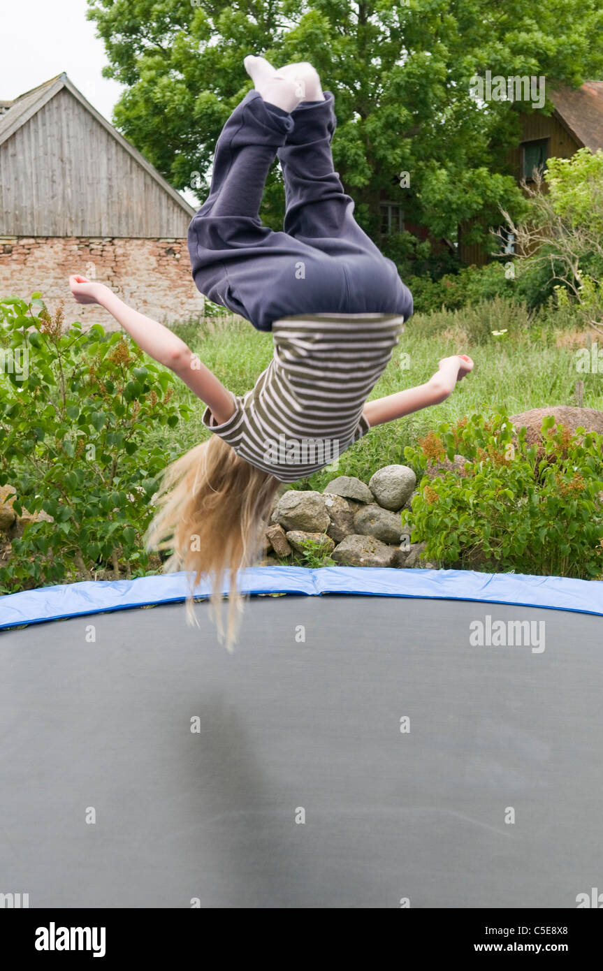 Rear view of a blond girl doing backflip on a trampoline with barn and  trees in the background Stock Photo - Alamy