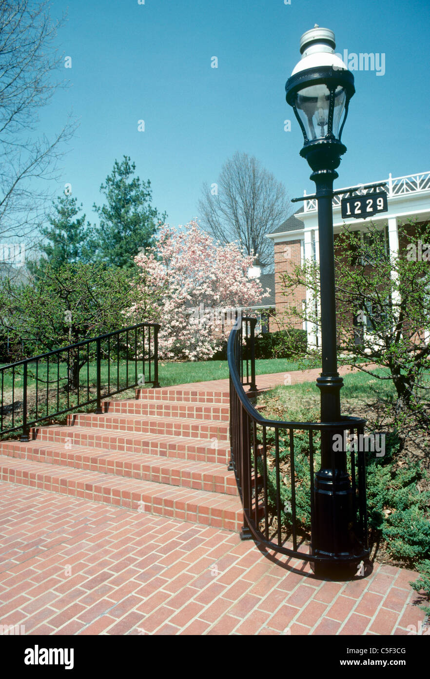 Brick front steps and wrought iron curved handrail with antique gas lamp welcome guests to formal home in early spring Stock Photo